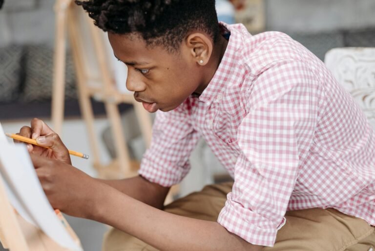 Teen boy drawing with focus in a creative indoor setting wearing checkered sleeves.